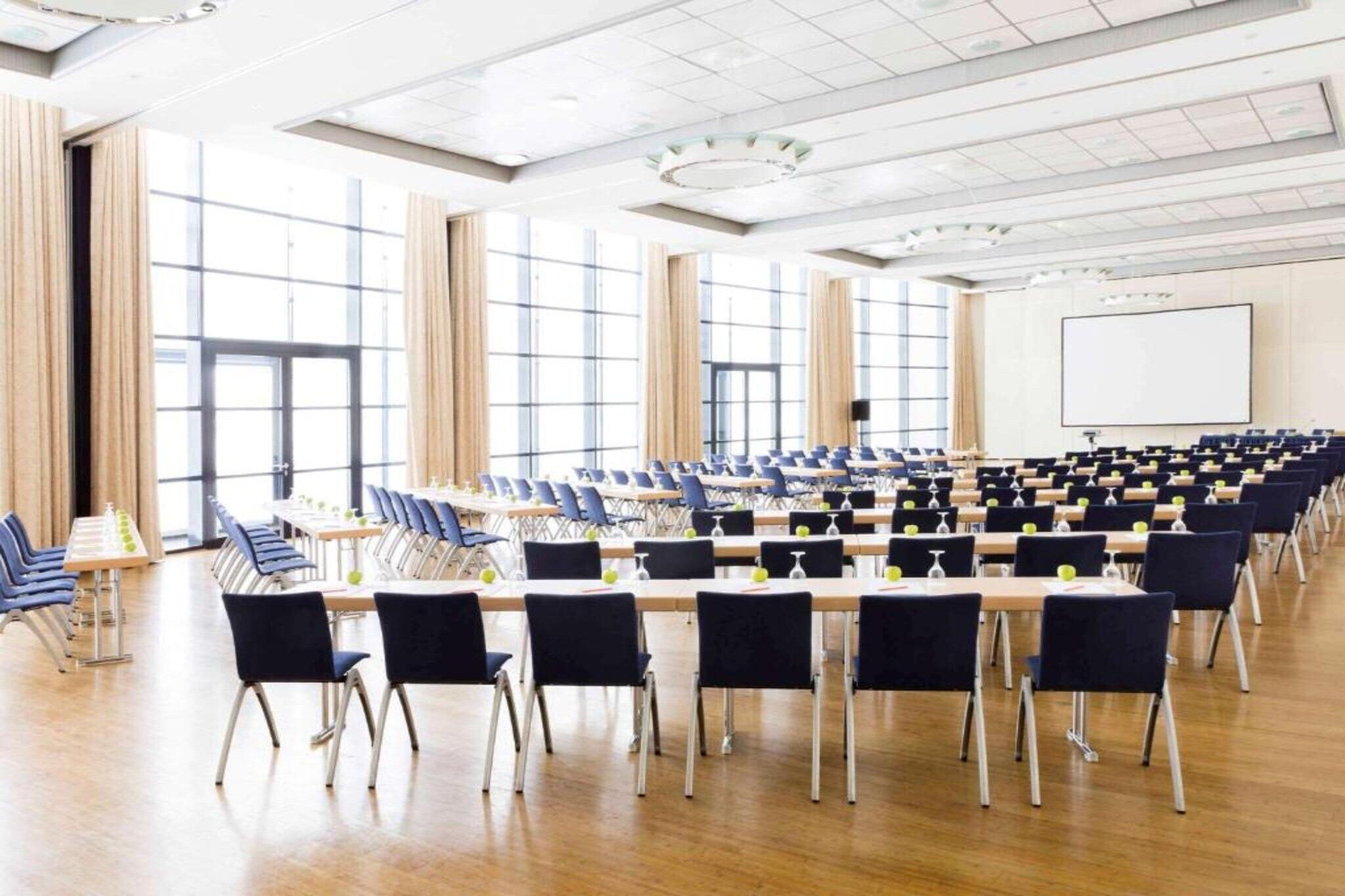 Ein Konferenzraum mit Tischen und Stühlen, großen Fenstern und einer Whiteboard-Wand.