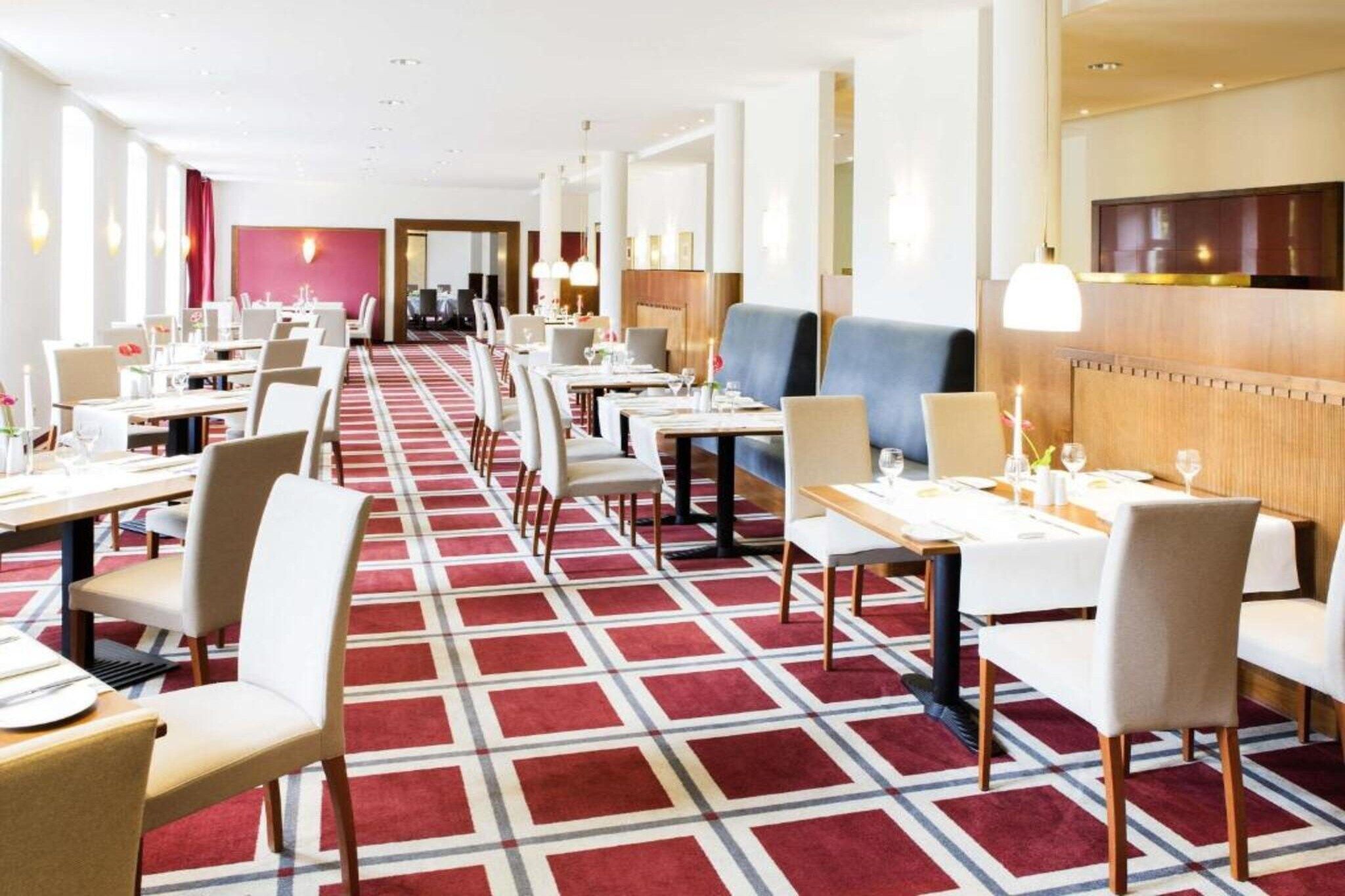 A hotel dining area with multiple tables and chairs, a patterned carpet, and a modern interior design.