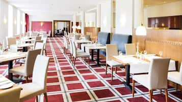 A hotel dining area with multiple tables and chairs, a patterned carpet, and a modern interior design.