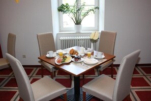 Un tavolo da pranzo con cibo per la colazione, sedie, una pianta in vaso e una finestra con vista.