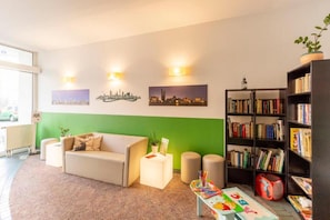 A living room with a sofa, a bookshelf, and a green accent wall. - Sunday Hotel Leipzig Südvorstadt (Markgraf) - Standard Single Room (Leipzig)