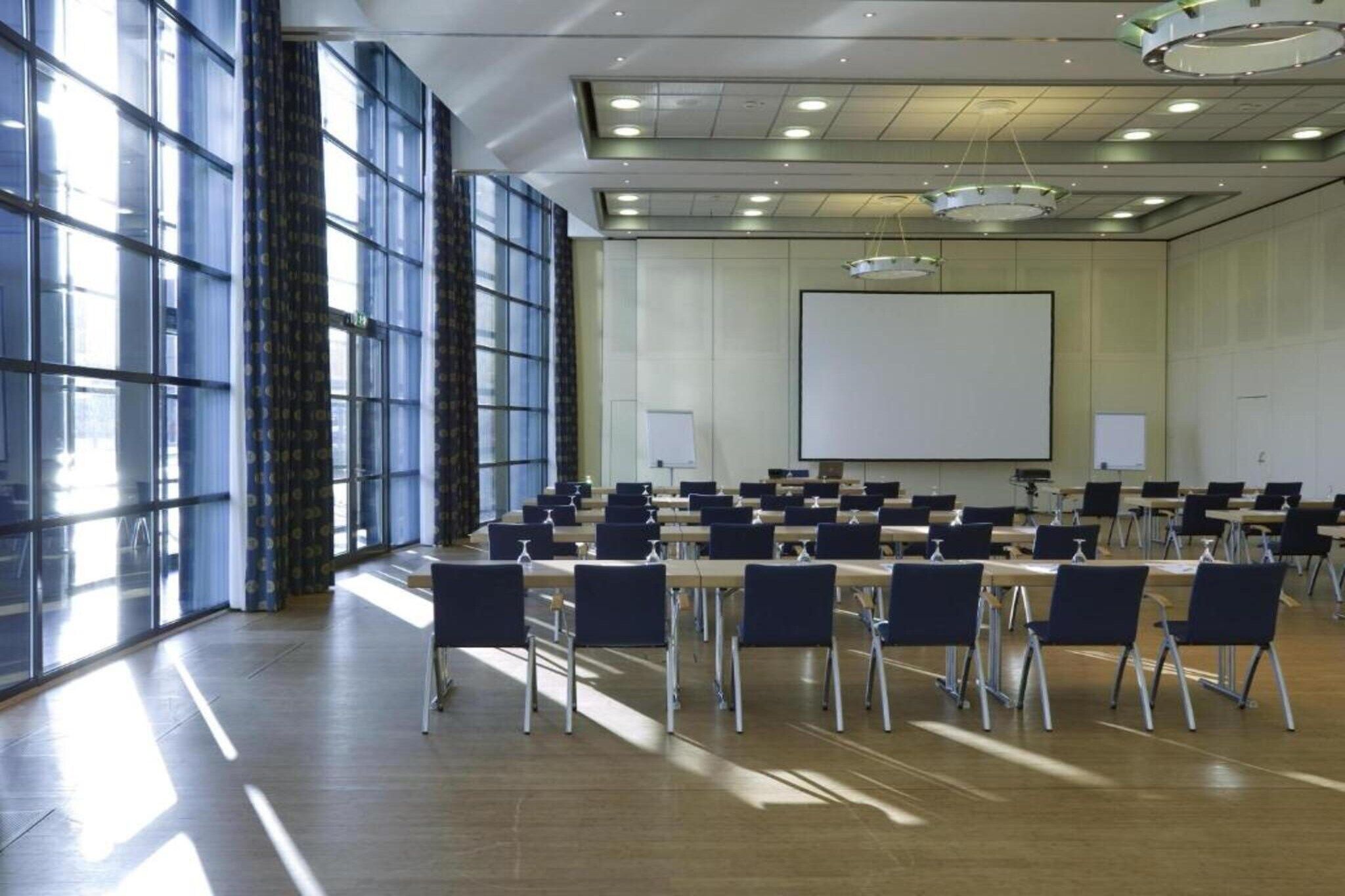 Ein Konferenzraum mit einem großen Bildschirm, mehreren Tischen und Stühlen, bereit für eine Besprechung.