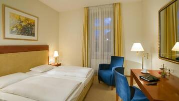 A hotel room with two beds, a desk with a chair, a lamp, a mirror, and a window with curtains.