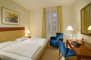 Habitació d'hotel amb dos llits, un escriptori amb cadira, una làmpada, un mirall i una finestra amb cortines.