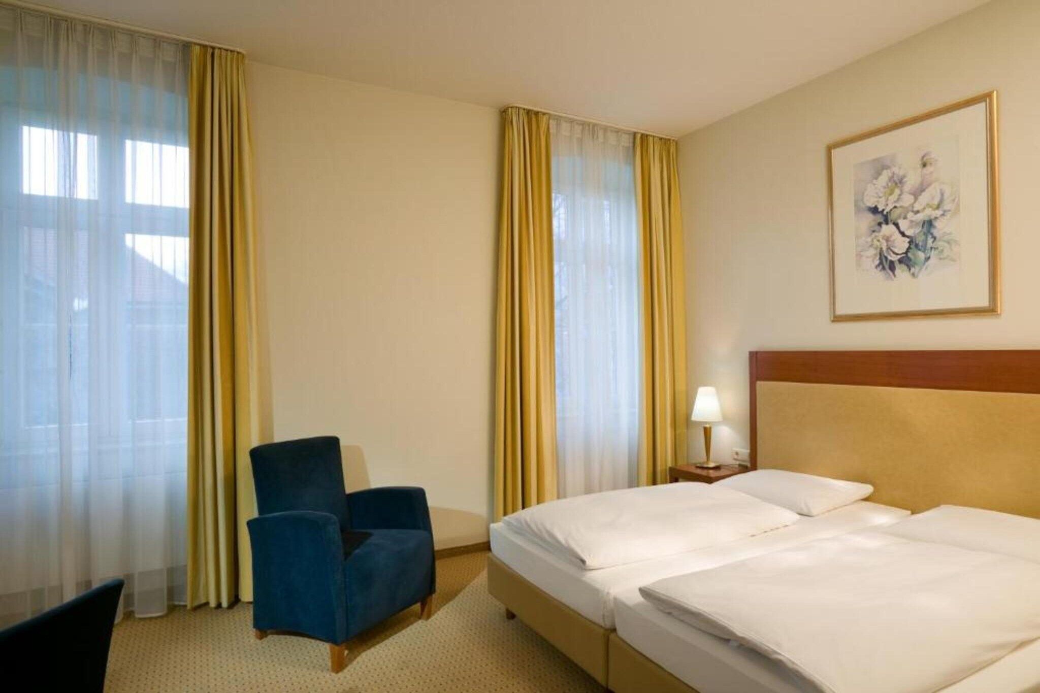 Ein Hotelzimmer mit einem Bett, einem Sessel, einem Nachttisch mit Lampe und einem Bild an der Wand.