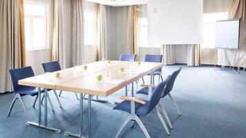 Ein Konferenzraum mit einem langen Tisch, blauen Stühlen, einer Whiteboard und einer Projektionsleinwand.