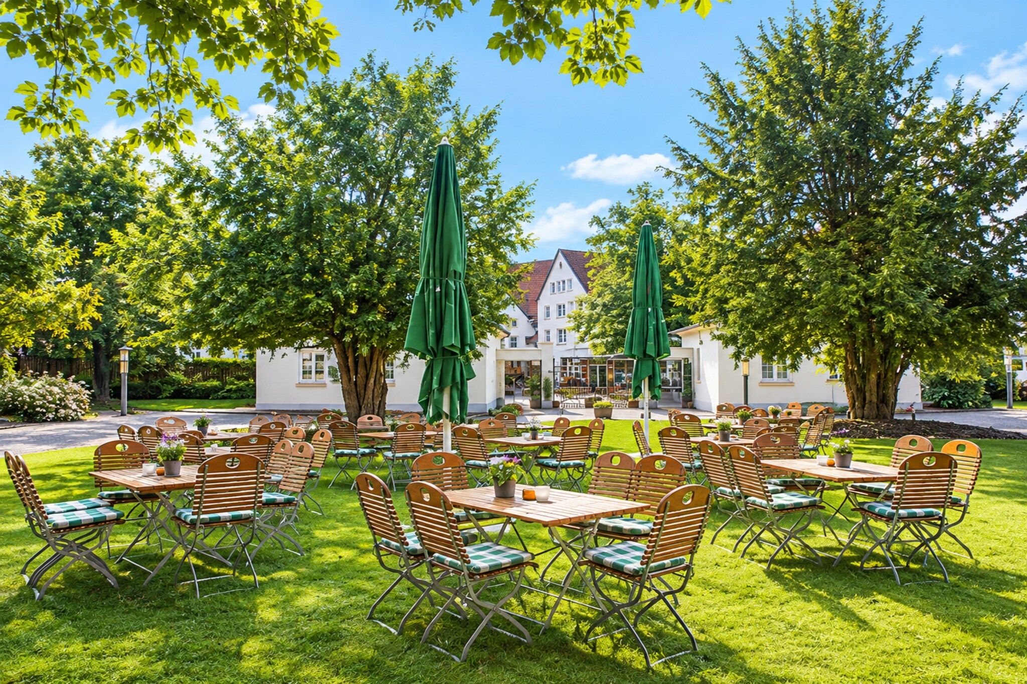 An outdoor seating area with tables and chairs, surrounded by trees and a building in the background.