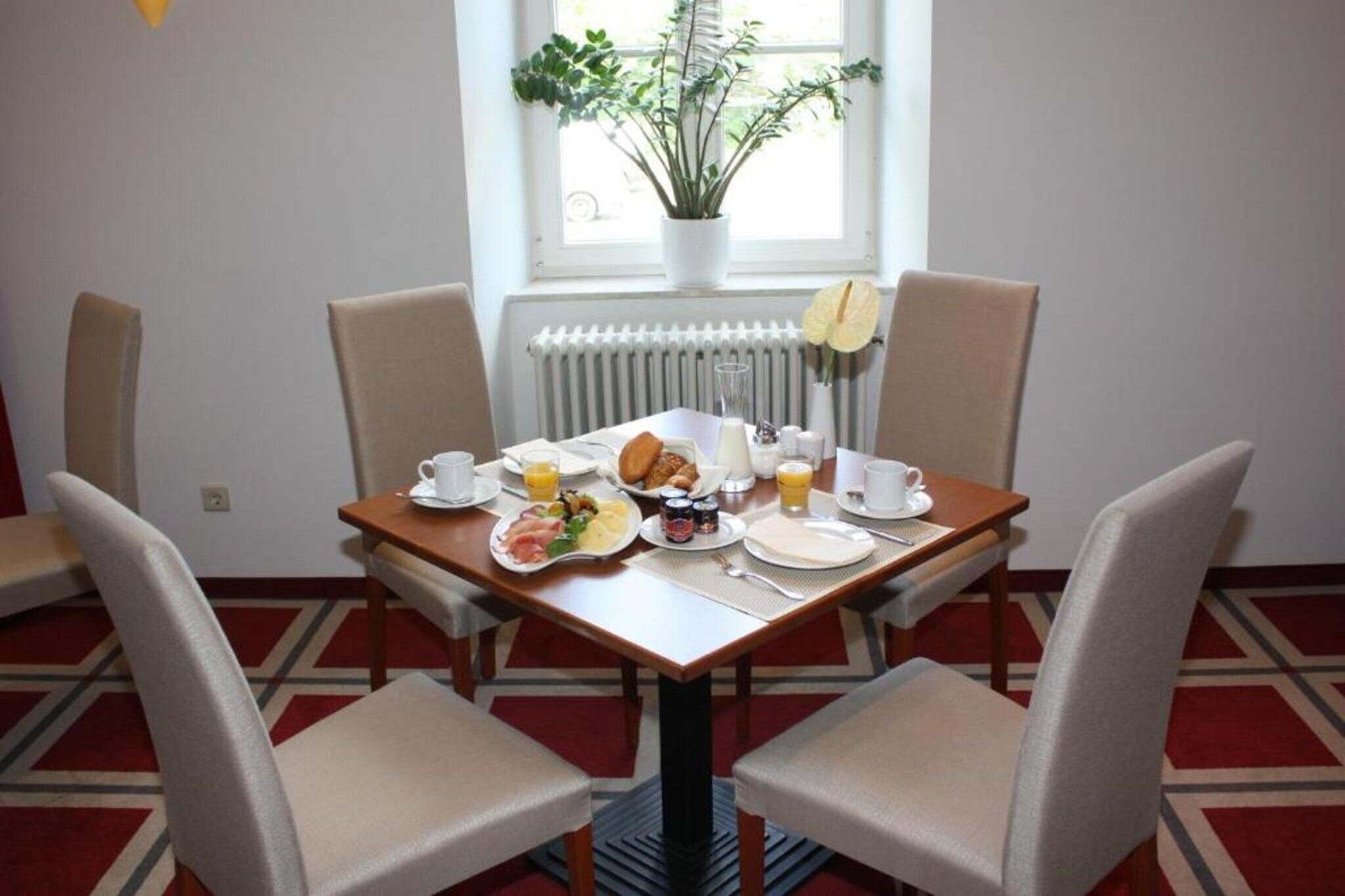 Ein Esstisch mit Frühstücksgebäck, Stühlen, einer Topfpflanze und einem Fenster mit Blick.