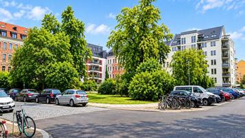Ein Parkplatz mit Autos und Fahrrädern, umgeben von Bäumen und Gebäuden mit mehreren Stockwerken und Balkonen.