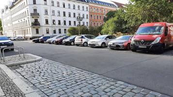 Eine Reihe geparkter Autos an einer Kopfsteinpflasterstraße, im Hintergrund ein Gebäude.