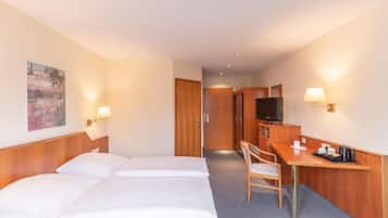 Ein Hotelzimmer mit zwei Betten, einem Schreibtisch mit Stuhl, einem Fernseher und einem Bild an der Wand.