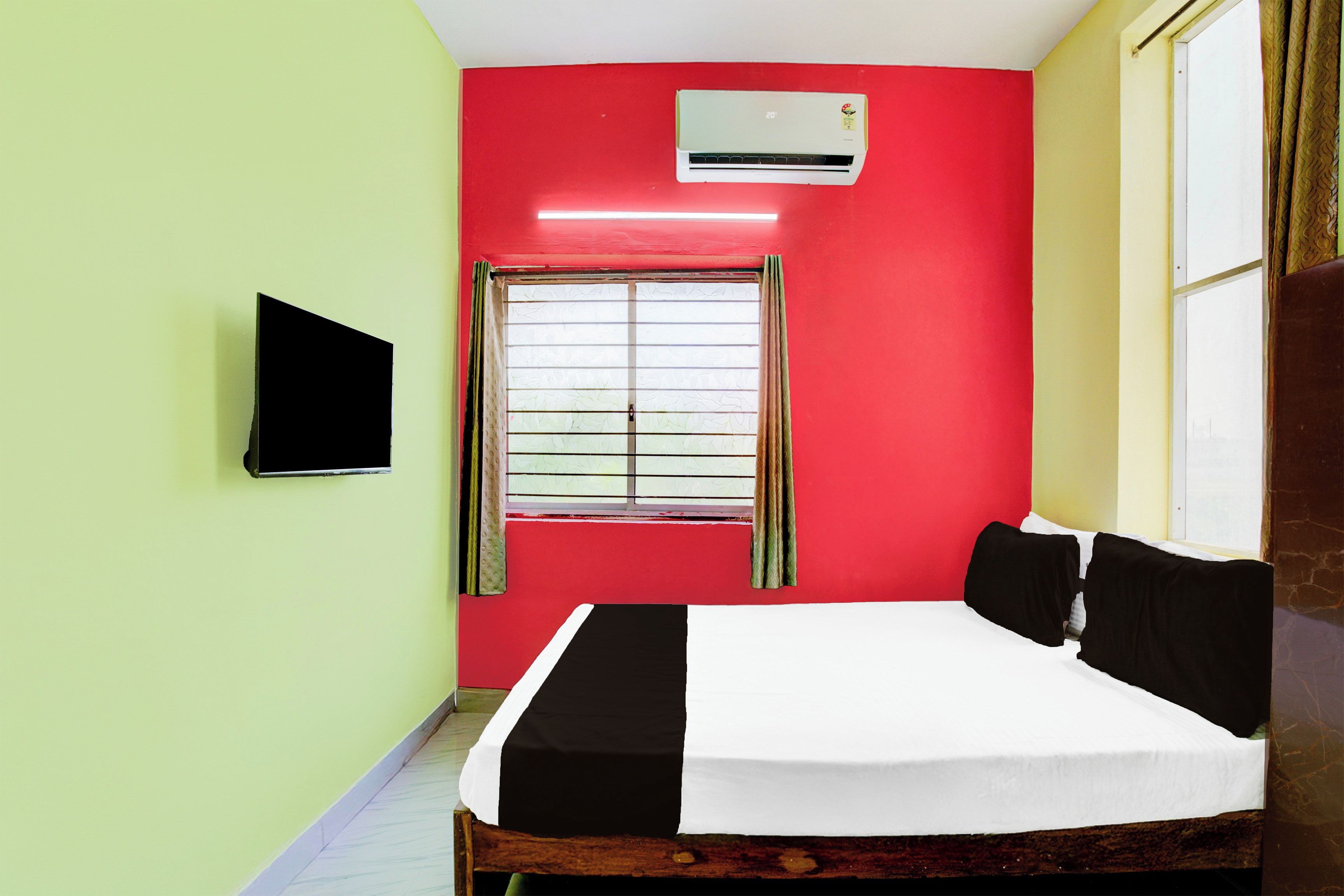 Una habitación con cama, ventana con cortinas, aire acondicionado y un televisor de pantalla plana montado en la pared.