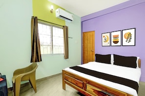Een slaapkamer met een bed, een stoel, een raam met gordijnen, een airconditioner en drie ingelijste foto's aan de muur.