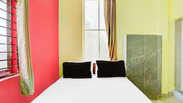 Una habitación con cama, dos almohadas, ventana con cortinas y armario.