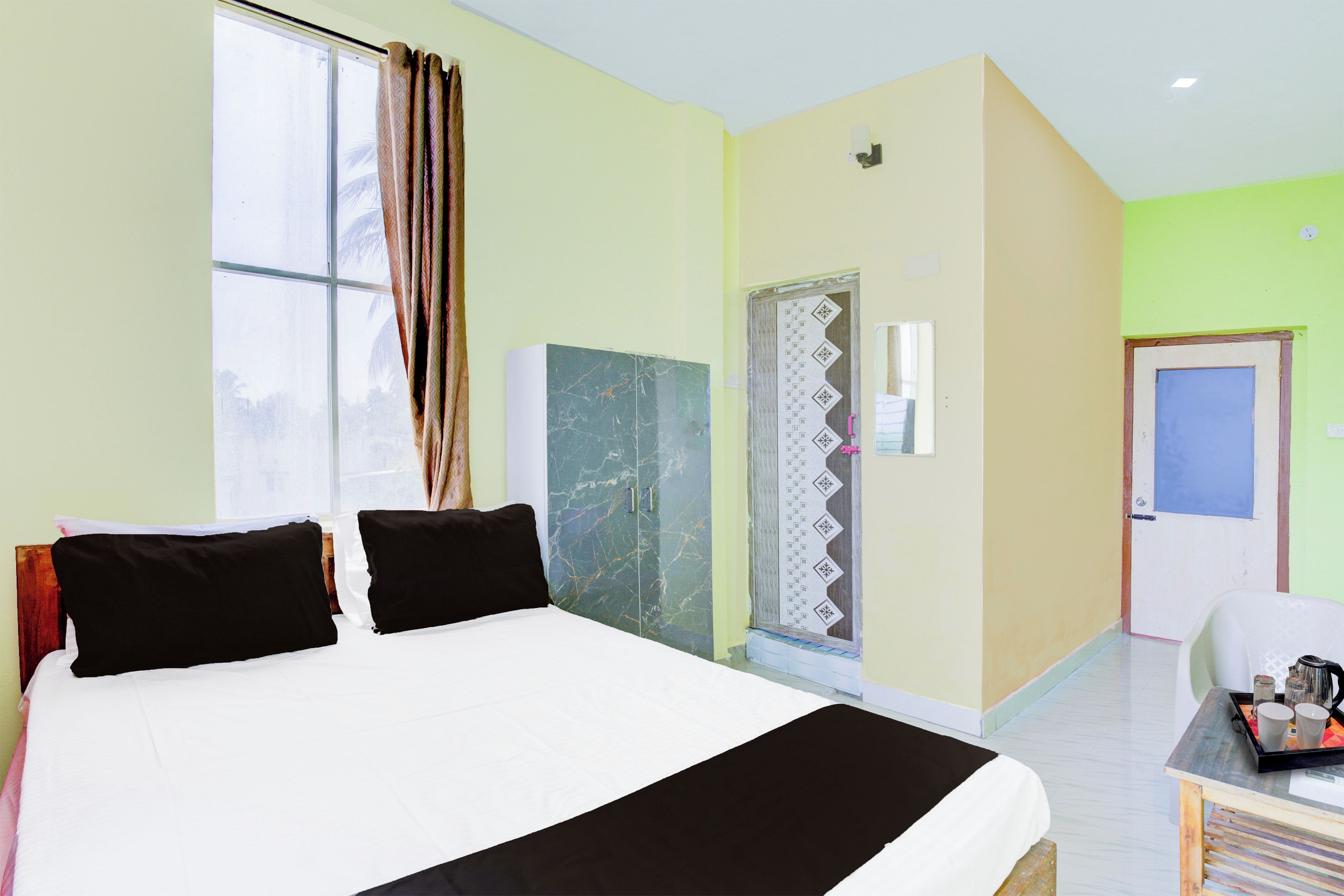 Habitación de hotel con una cama grande, un escritorio con bandeja, una puerta y una ventana con cortinas.
