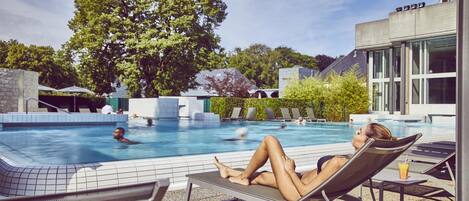Un área de piscina con sillones de descanso, una piscina y un árbol grande.