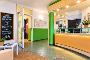 A hotel reception area with a green wall, a reception desk, a map on the wall, and a sign with text.