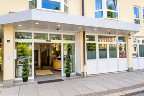 A hotel entrance with a covered entrance, glass doors, and potted plants.