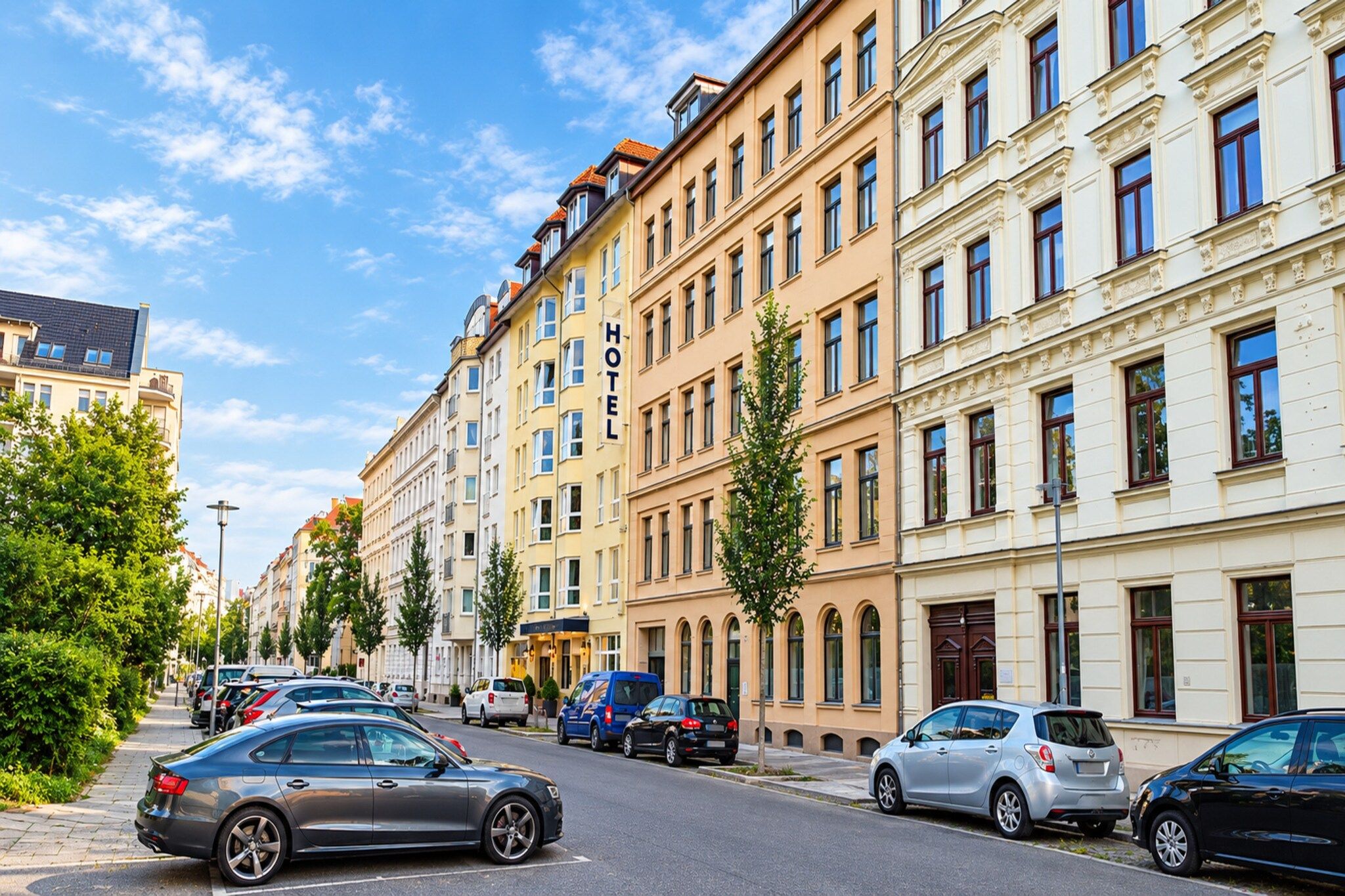 A hotel building with multiple floors, a clear sky, and parked cars along the street.