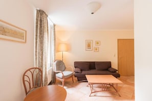 A living room with a brown sofa, a wooden dining table, a striped chair, and a lamp. - Sunday Hotel Leipzig Südvorstadt (Markgraf) - Family Room (Leipzig)