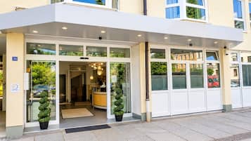 A hotel entrance with a covered entrance, glass doors, and potted plants.