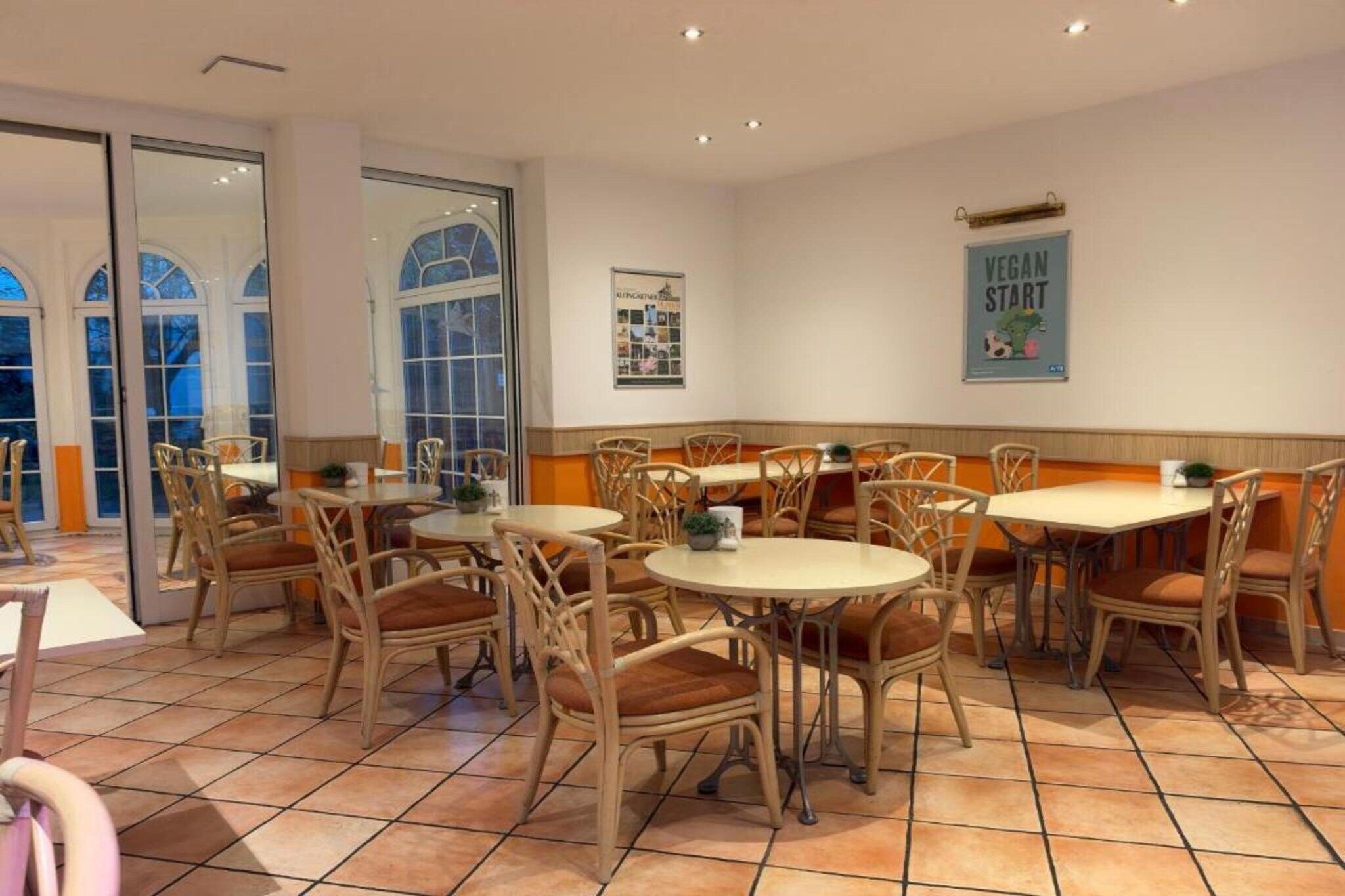 A restaurant interior with round tables and wicker chairs, a tiled floor, and a poster on the wall.
