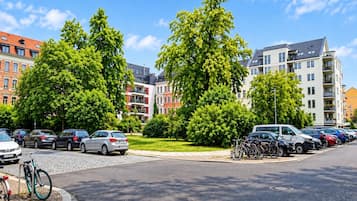 Un área de estacionamiento con autos y bicicletas, rodeada de árboles y edificios con varios pisos y balcones.