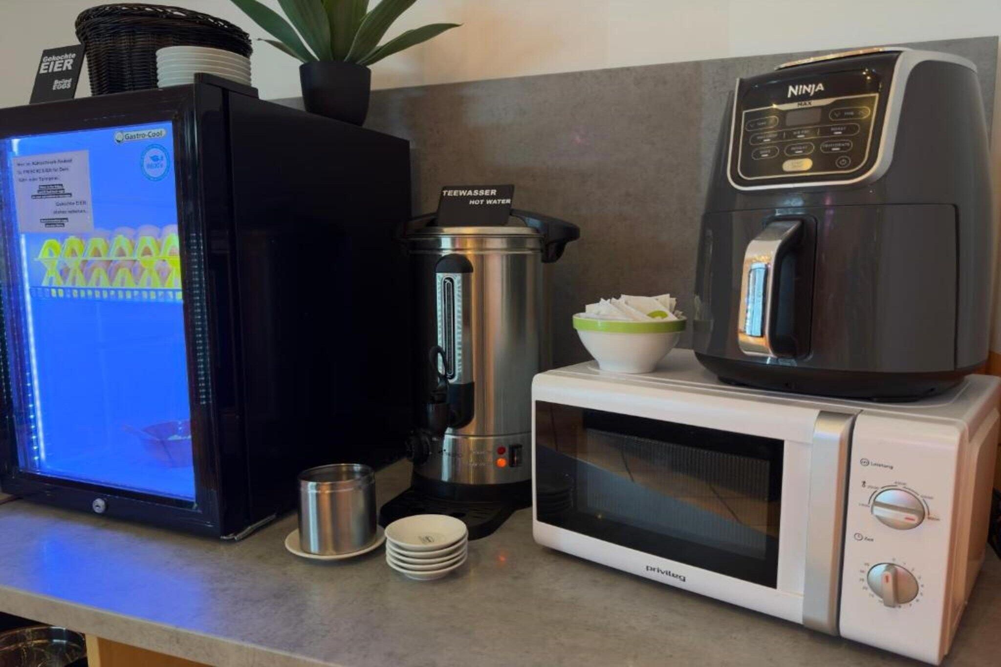 Eine Küche mit Kaffeemaschine, Mikrowelle, Wasserkocher und einem Computermonitor, der eine Speisekarte zeigt.