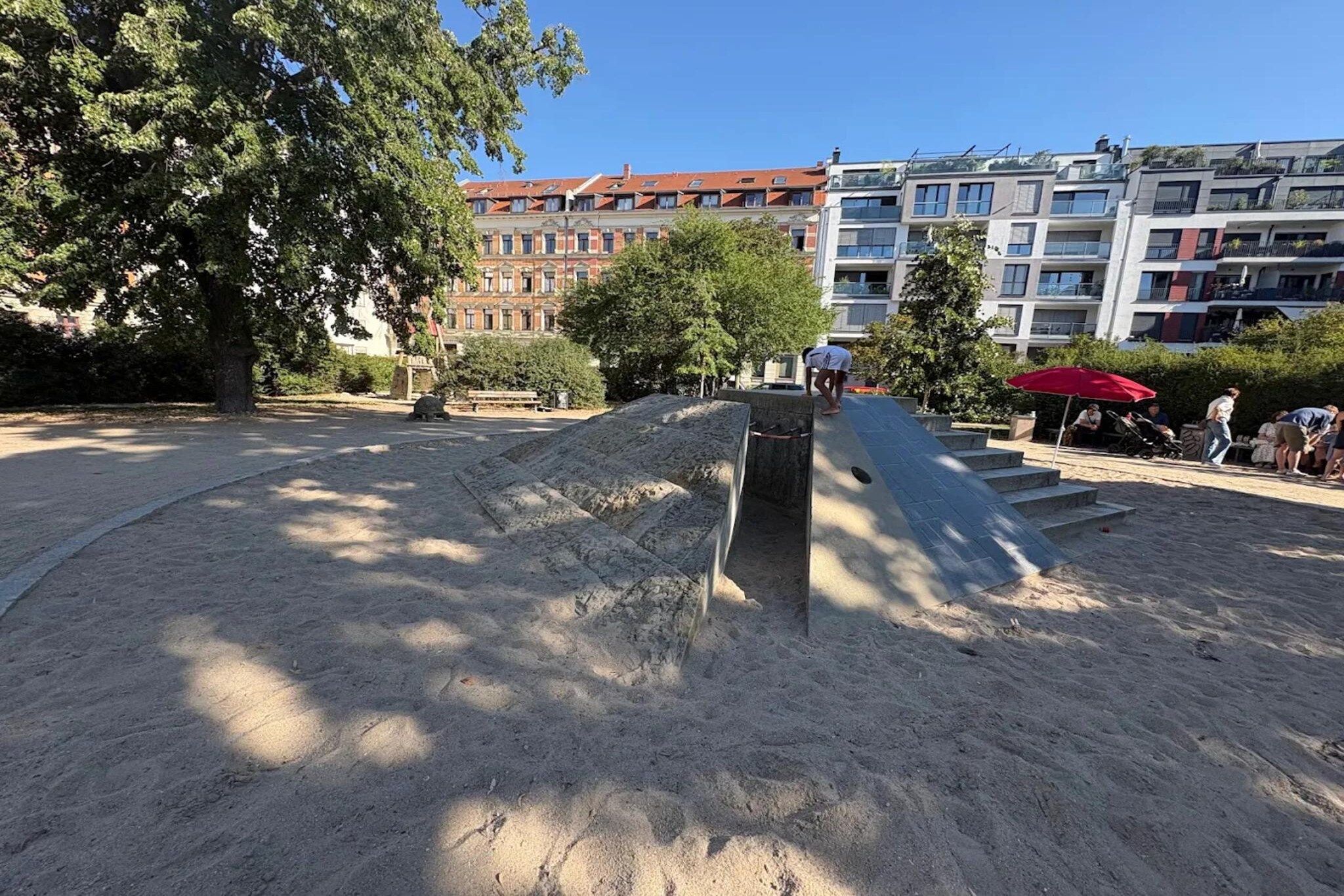 A sandy area with a concrete structure, trees, and buildings in the background.
