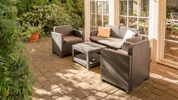 An outdoor patio with wicker furniture, including a sofa, chairs, and a coffee table.