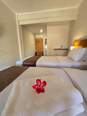 A hotel room with two beds, a nightstand, and a bathroom visible in the background. - Hotel Ikhtiar Surya (Banyuwangi)