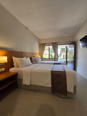 A hotel room with a bed, bedside table, and a view of the outdoors. - Hotel Ikhtiar Surya (Banyuwangi)