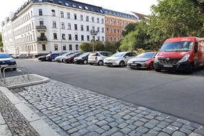 Eine Reihe geparkter Autos an einer Kopfsteinpflasterstraße, im Hintergrund ein Gebäude.
