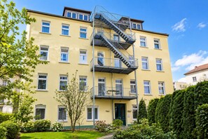Ein mehrstöckiges Gebäude mit Feuerleiter, Balkonen und einem gepflegten Garten.