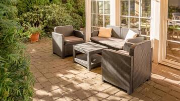 An outdoor patio with wicker furniture, including a sofa, chairs, and a coffee table.