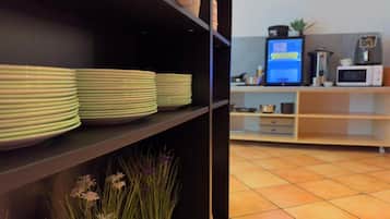 Et køkken med stablede tallerkener på hylder, en computorskærm, en mikrobølgeovn og en lille plante.