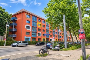 Un edificio de varios pisos con balcones, una señal de calle, autos estacionados y una señal de paso de peatones.