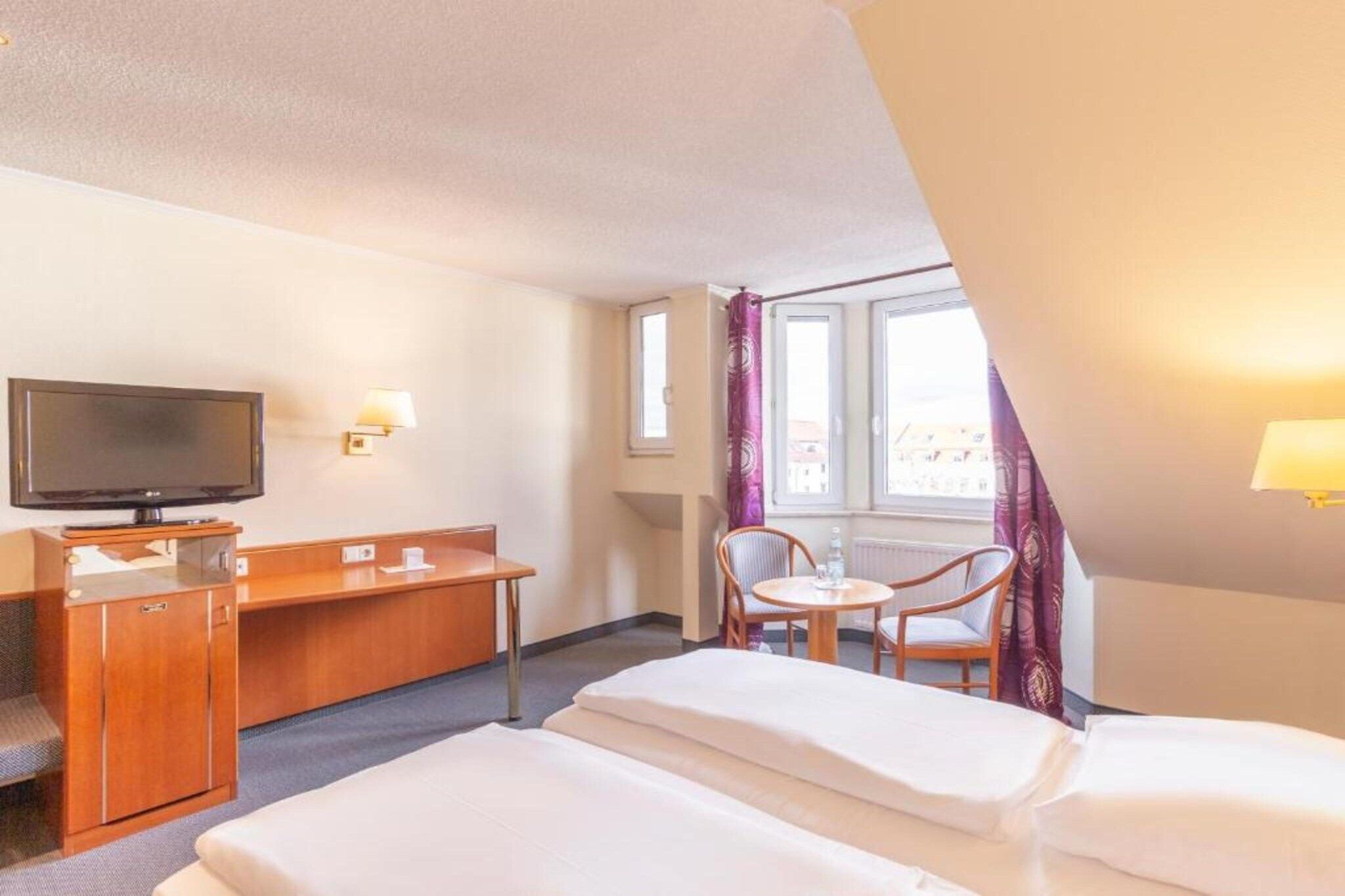 A hotel room with a bed, a desk, a television, and a window with curtains.