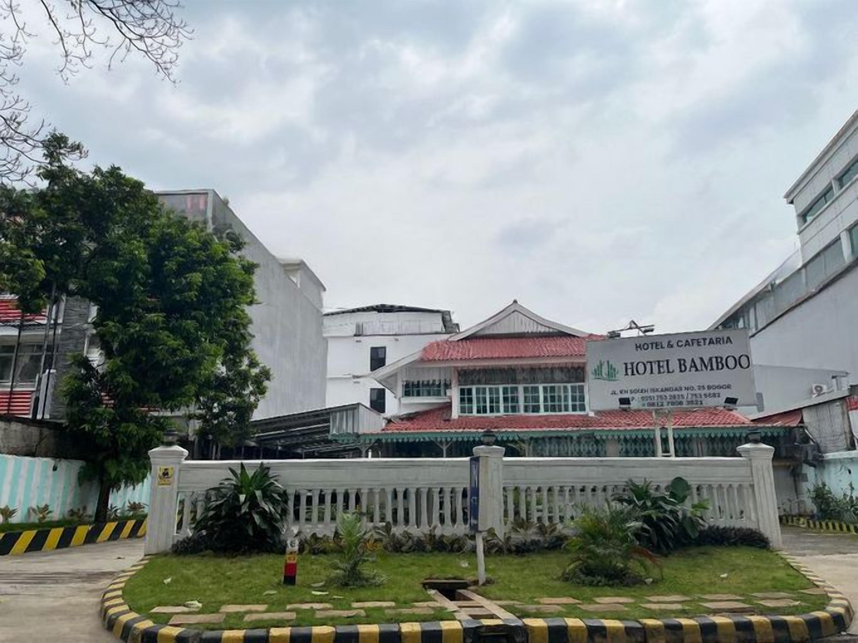 A hotel with a red-tiled roof, a white fence, and a signboard.