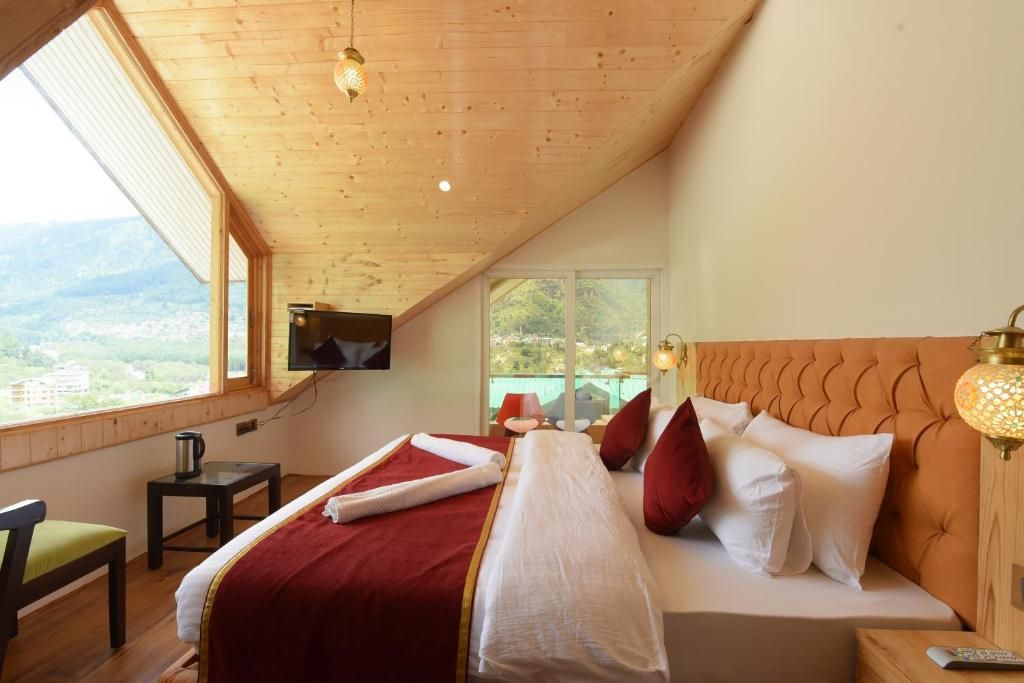 A bedroom with a bed, a TV mounted on the wall, a window with a view, and a bedside table with a lamp.