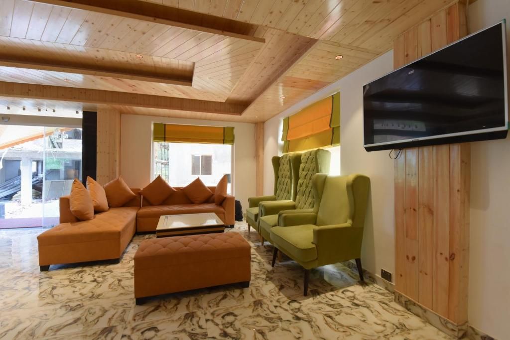 A modern living room with a sectional sofa, a green armchair, and a flat-screen TV mounted on the wall.