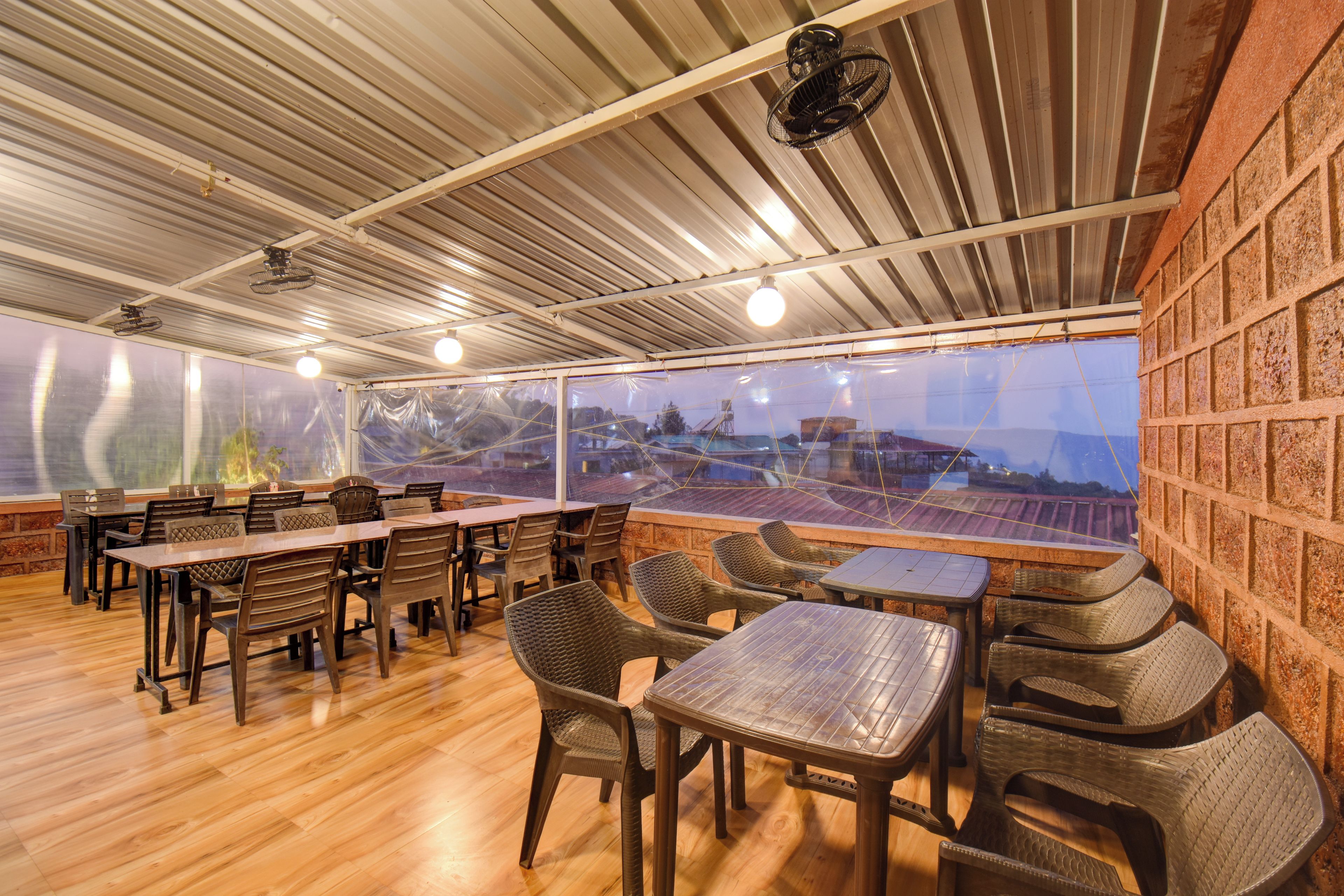 An outdoor seating area with tables and chairs, a view of a distant landscape, and a metal roof structure.