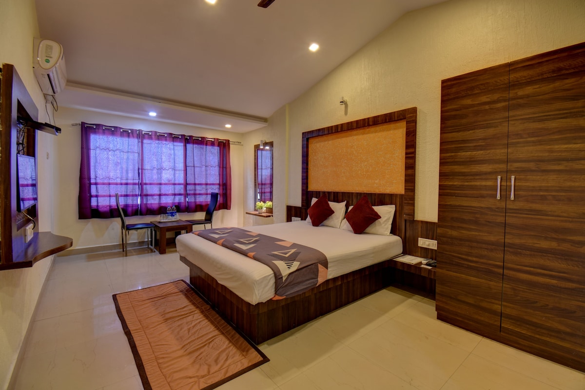 A hotel room with a bed, a desk, a chair, a wardrobe, and a window with curtains.