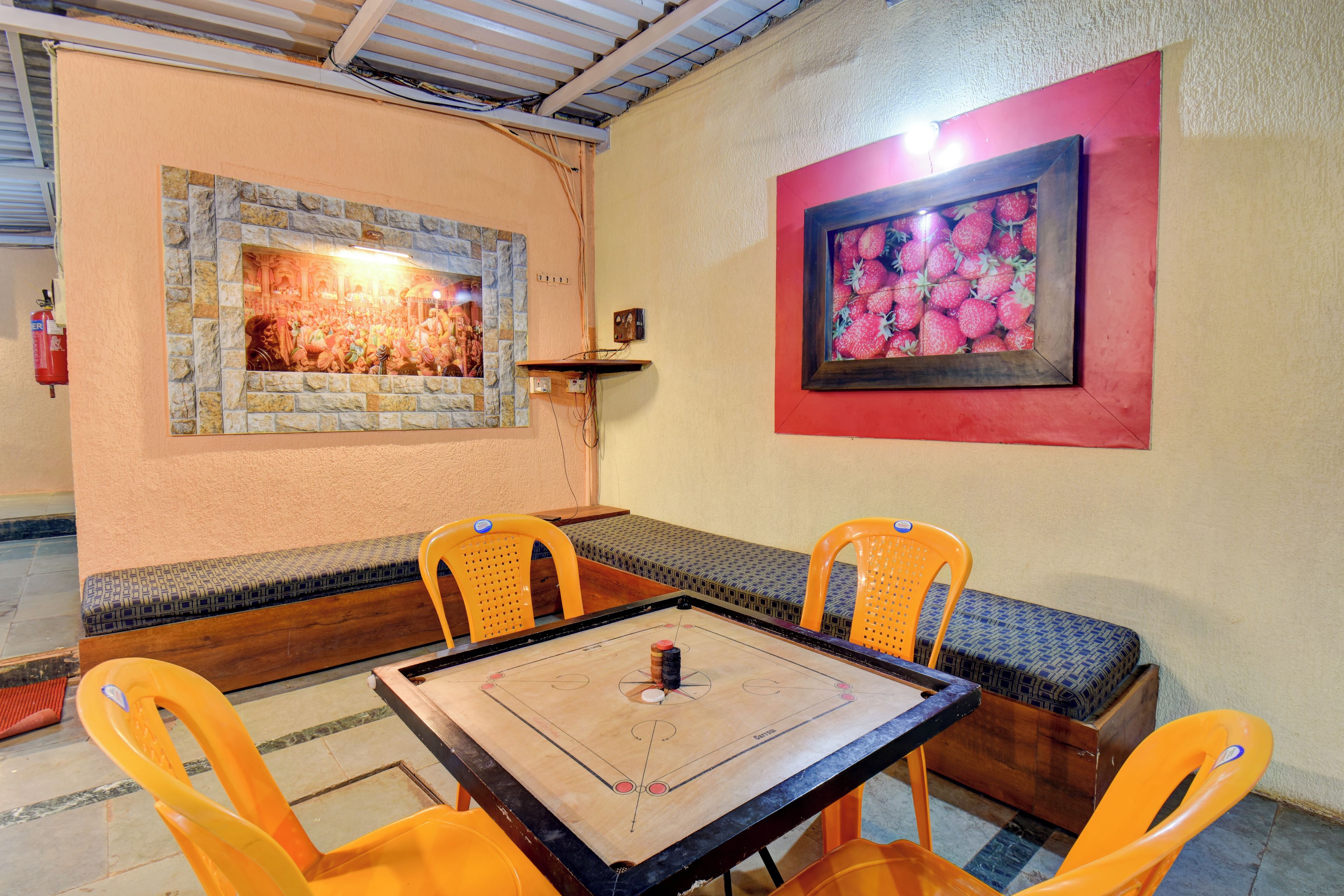 Quarto com mesa de madeira, quatro cadeiras laranja, um banco e duas molduras nas paredes.