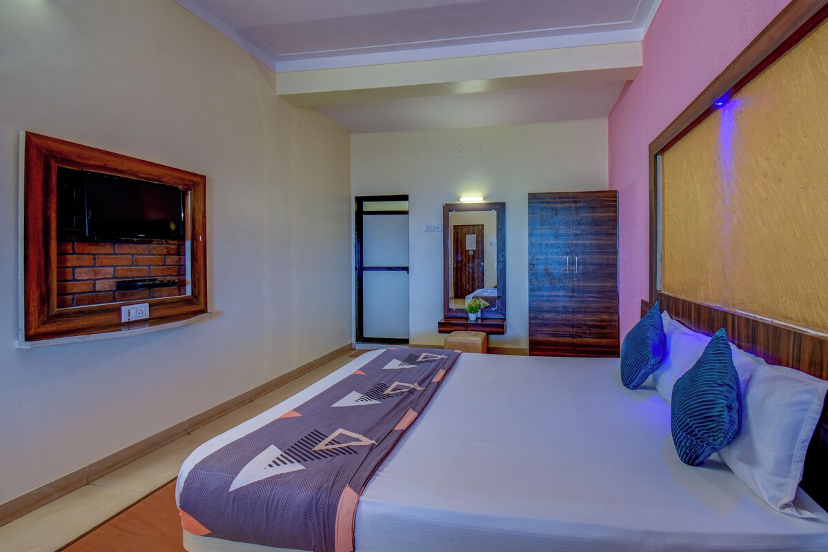 A hotel room with a bed, a television mounted on a brick wall, a door leading to another room, and a wall with a decorative panel.