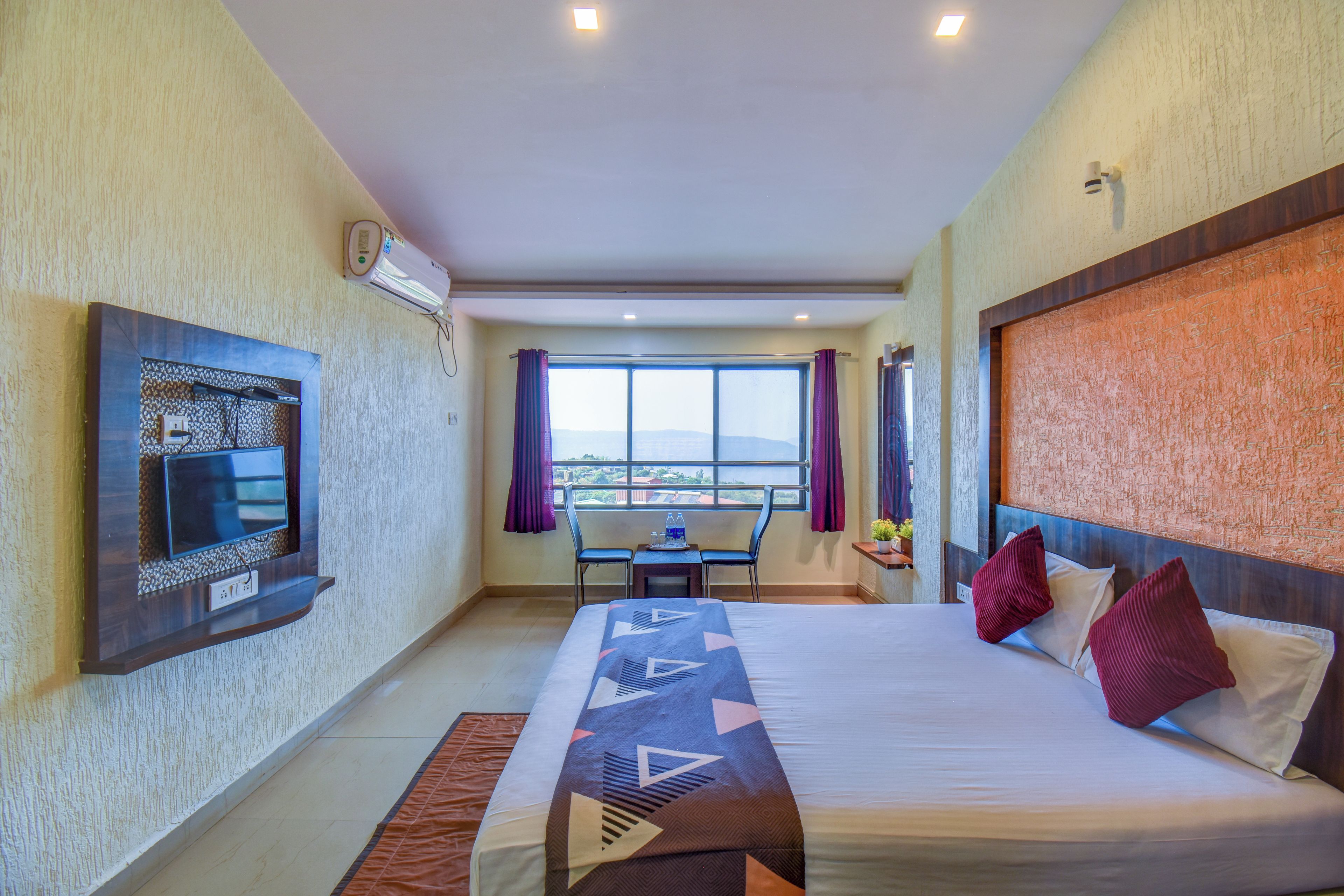 Une chambre d’hôtel avec un lit, un téléviseur fixé au mur, une fenêtre avec des rideaux et une vue sur l’extérieur.