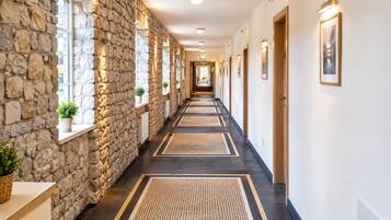 A hotel hallway with stone walls, wooden doors, and a central walkway.