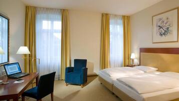 A hotel room with a desk, two chairs, a bed, and a painting on the wall.
