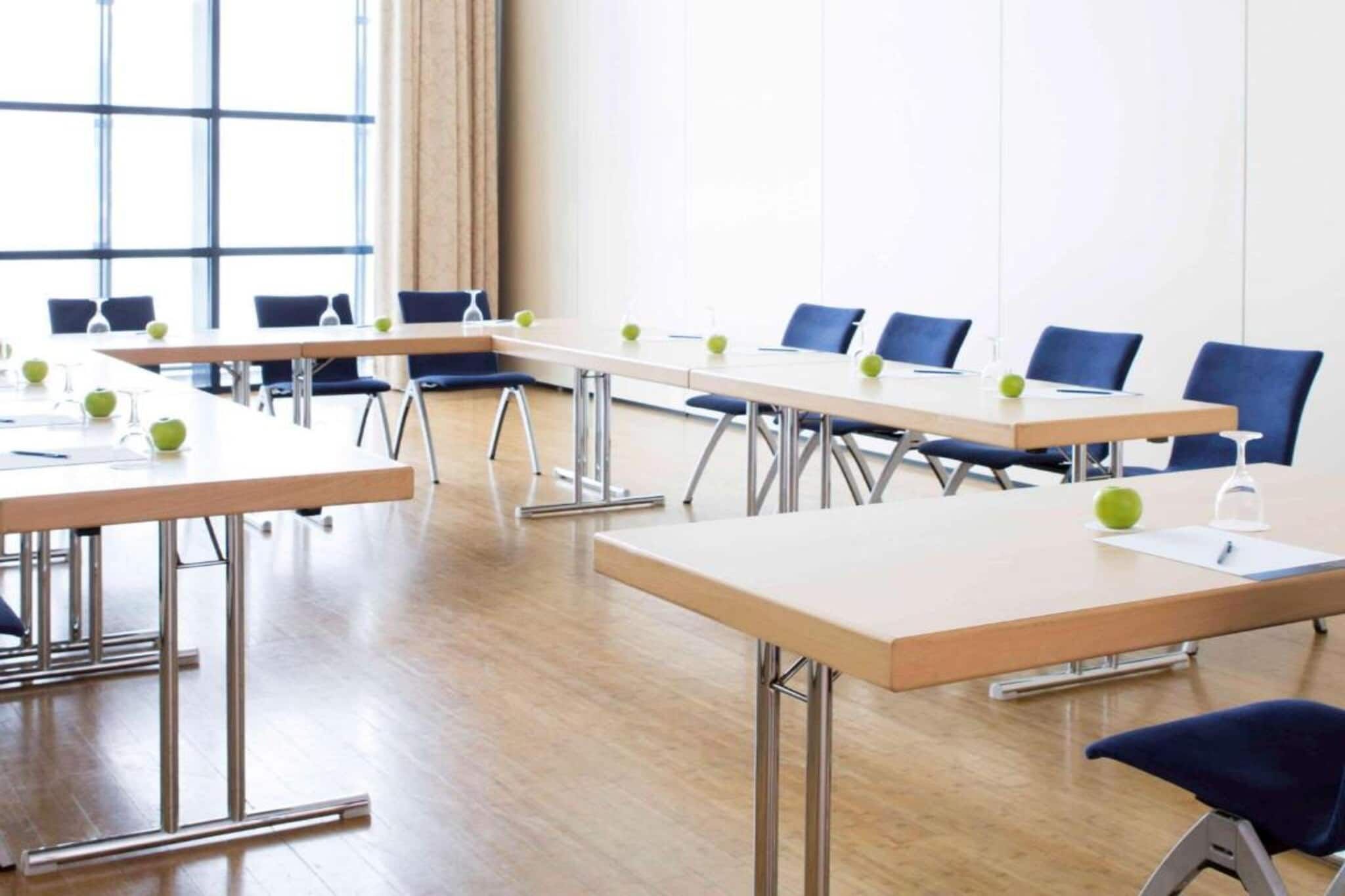 A conference room with long tables, chairs, and green apples on the tables.