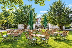 An outdoor seating area with tables and chairs, surrounded by trees and a building in the background. - Sunday Hotel Hildesheim Zentrum - Double room (Hildesheim)